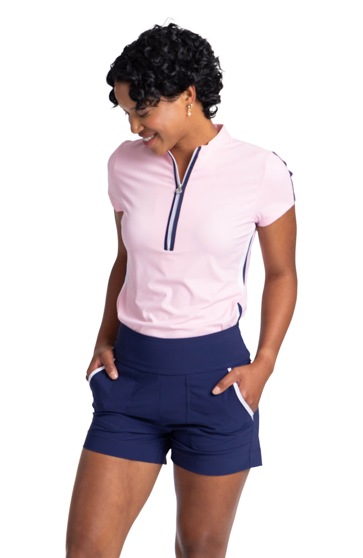 A woman wearing a soft pink, short sleeve top. The top has a navy blue stripe going down the middle of the sleeve and contrasting white and navy blue stripes going down the side. The top is worn with navy blue shorts with white trim on the side pockets. 