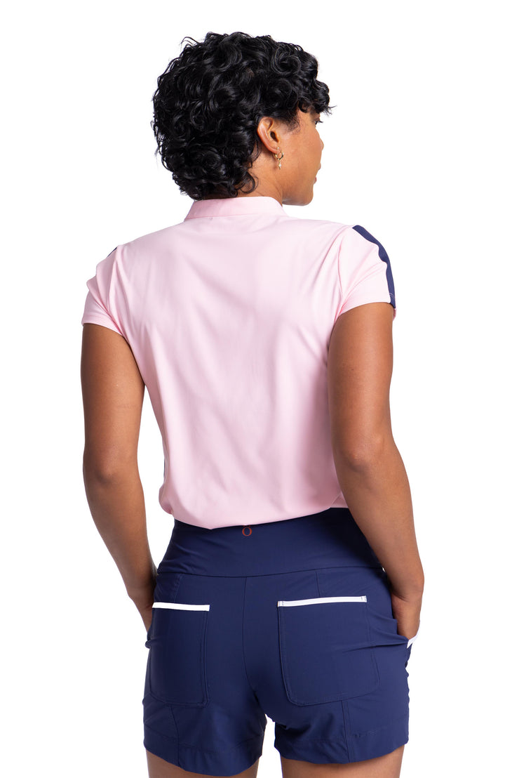 Back view of a woman wearing a soft pink, short sleeve top and navy blue shorts with white trim on the back pockets. 